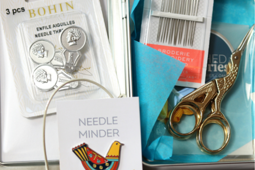 stitcher's tin filled with scissors, needles, needle threaders and a needle minder 
