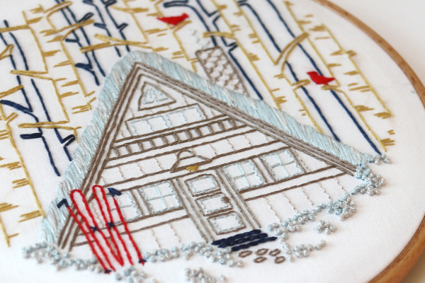closeup of embroidery project with french knots as snow on winter cabin scene