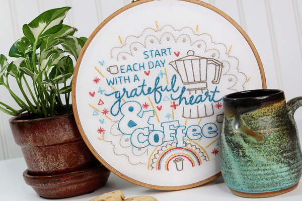 coffee-themed embroidery hoop displayed with houseplant and decorative mug.