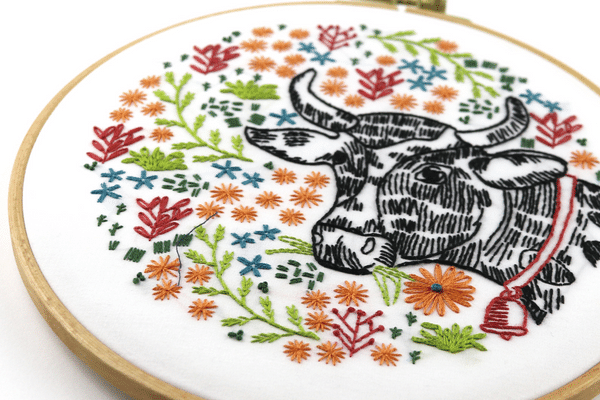 embroidery hoop-art with cow surrounded by flowers.