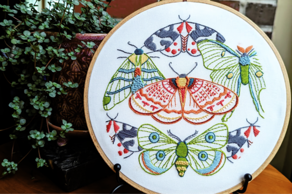 Embroidered hoop art of moths displayed on stand.