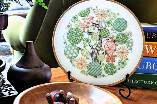 Embroidered hoop art of tree of life displayed on stand.