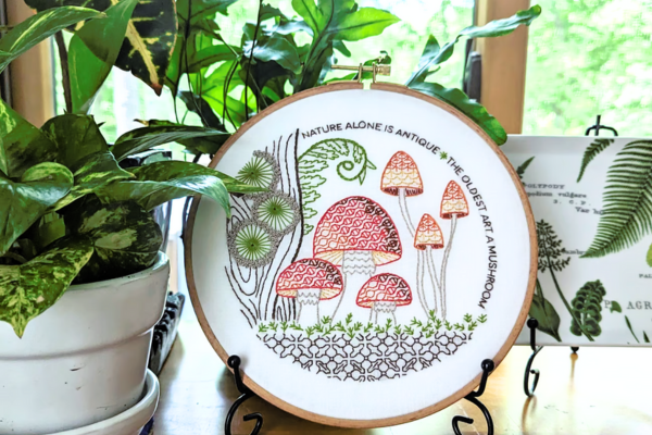 Embroidered hoop art of small birds displayed on stand.
