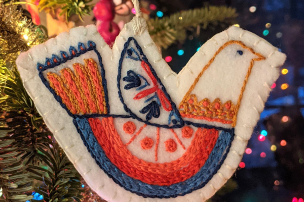 Embroidered holiday folk-art bird ornament hanging from Christmas tree