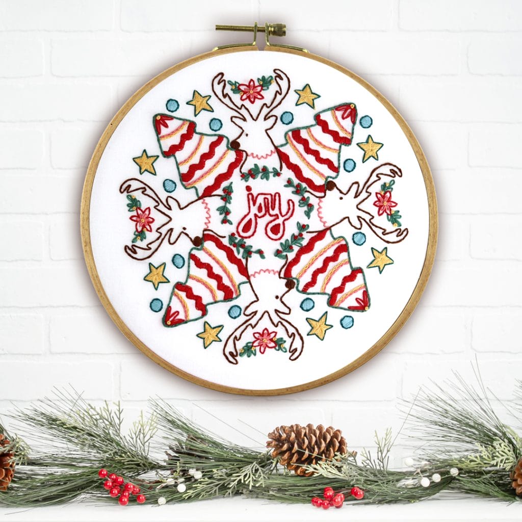 Whimsical reindeer Christmas embroidery hung over pine boughs and holiday mantle.